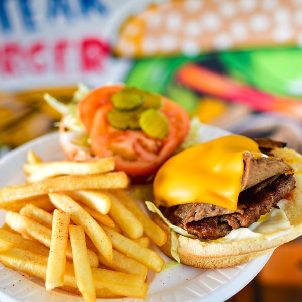 A Canada Steak Burger with cheese, lettuce, tomato, pickles, and fries on a white plate.