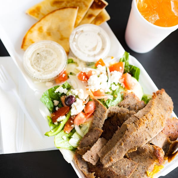 Canada Steak Burger's gyro plate with sliced meat, Greek salad, pita bread, and a drink.