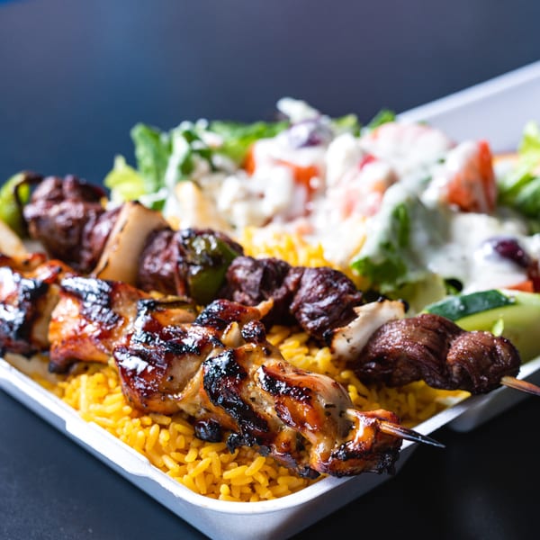 Two grilled skewers, one chicken and one beef, with yellow rice and a side salad.